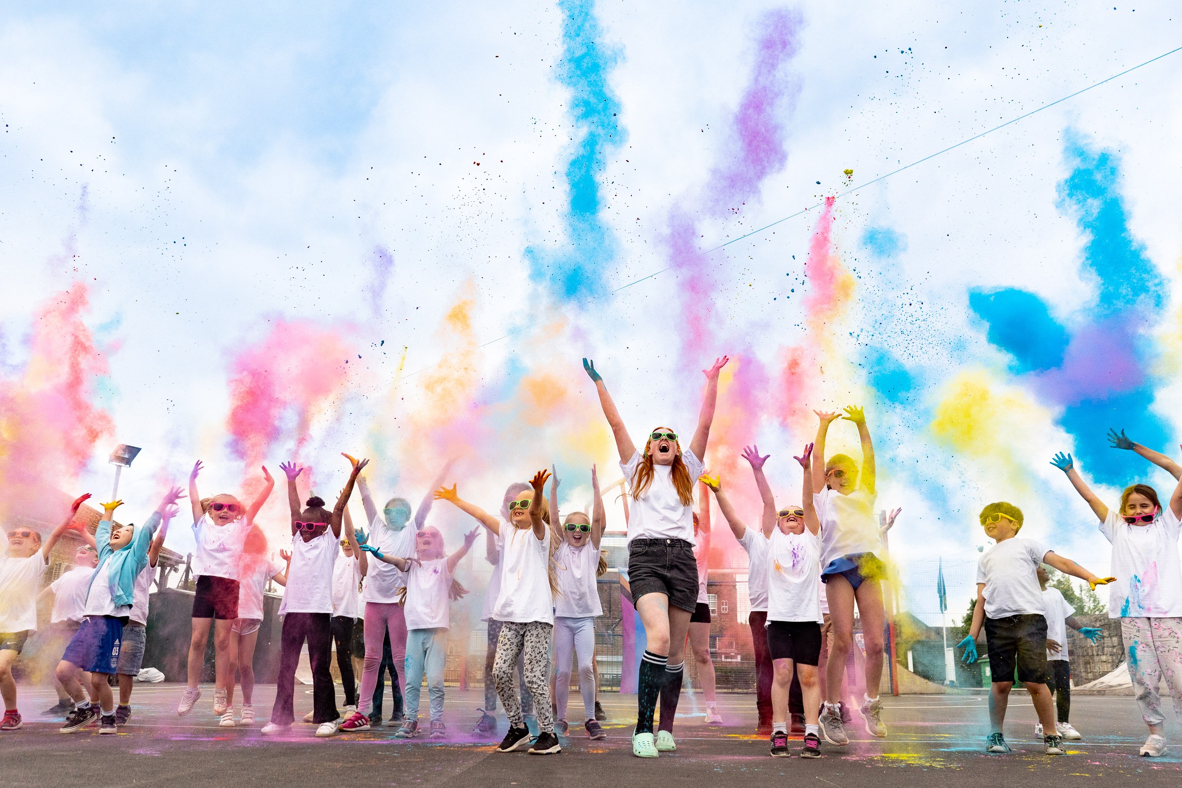 A group of delighted and joyful children in white t-shirts throwing paint bombs up into the air.
